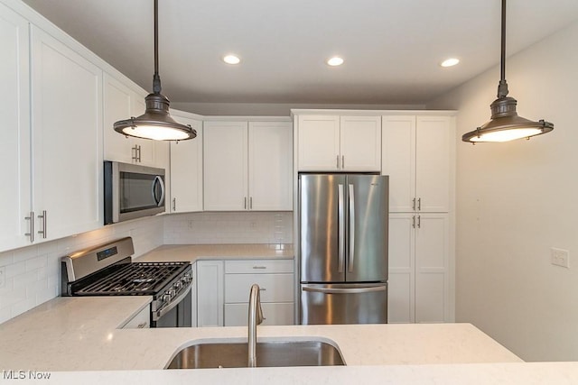 kitchen featuring stainless steel appliances, white cabinetry, sink, and decorative light fixtures