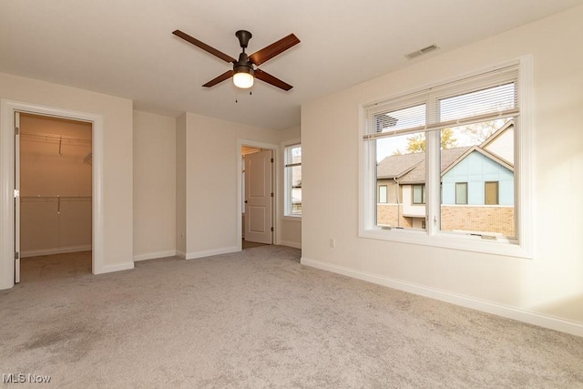 unfurnished bedroom with light carpet, a walk in closet, a closet, and ceiling fan