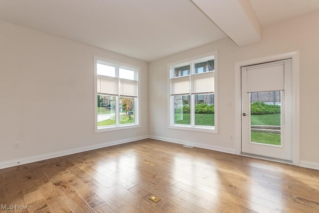 unfurnished room featuring beamed ceiling and light wood-type flooring