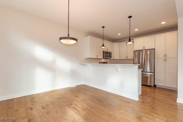 kitchen with decorative light fixtures, white cabinetry, light hardwood / wood-style floors, kitchen peninsula, and stainless steel appliances