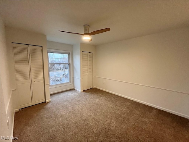 unfurnished bedroom with dark carpet, ceiling fan, and two closets