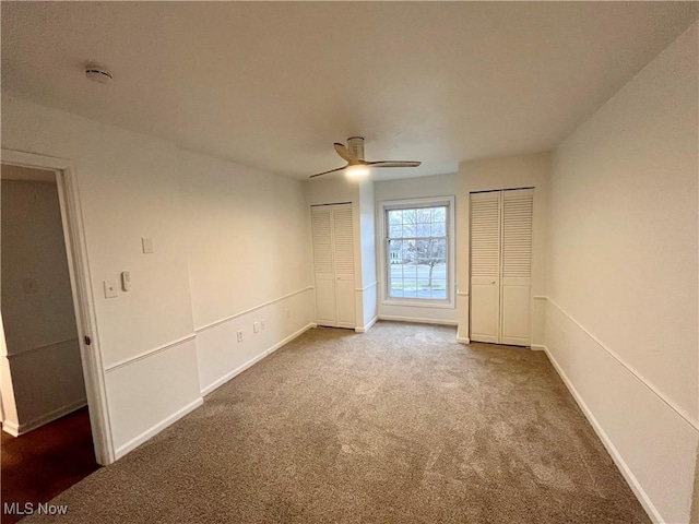 empty room with carpet, ceiling fan, and multiple closets