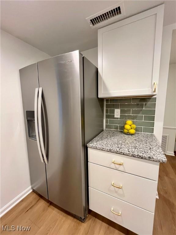 kitchen featuring white cabinetry, stainless steel refrigerator with ice dispenser, light stone countertops, light hardwood / wood-style floors, and tasteful backsplash