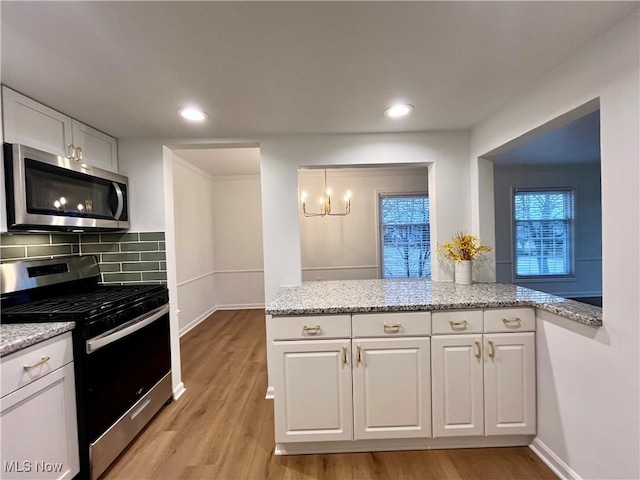 kitchen featuring appliances with stainless steel finishes, white cabinetry, light stone counters, and light hardwood / wood-style flooring