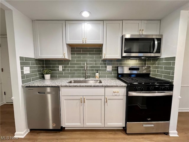 kitchen with sink, stainless steel appliances, white cabinets, and light stone counters