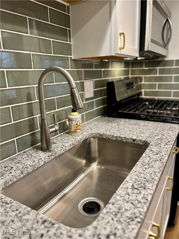 details featuring sink, light stone counters, stove, and decorative backsplash