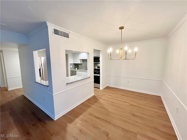 unfurnished dining area featuring light hardwood / wood-style flooring, sink, a chandelier, and crown molding