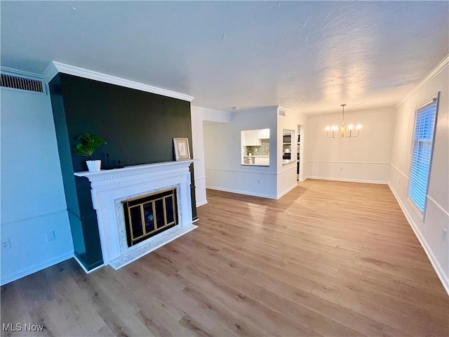 unfurnished living room featuring ornamental molding, light wood-type flooring, and a chandelier