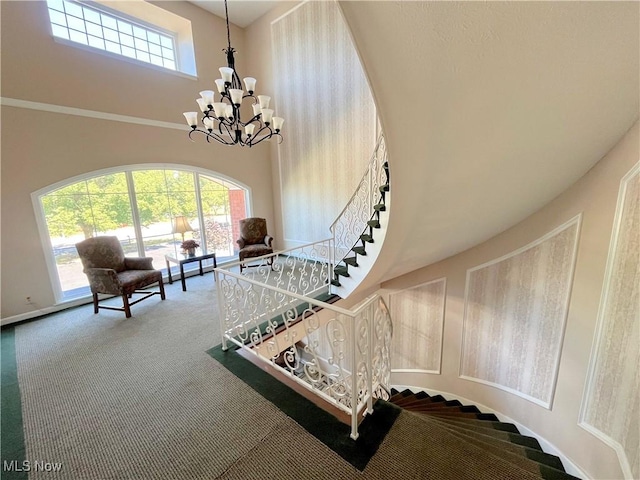 stairs with a wealth of natural light, carpet floors, a towering ceiling, and an inviting chandelier