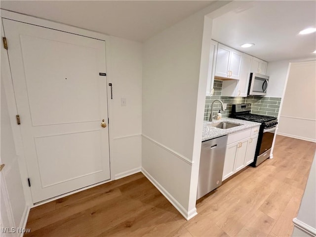 kitchen featuring white cabinetry, light wood-type flooring, sink, light stone counters, and appliances with stainless steel finishes