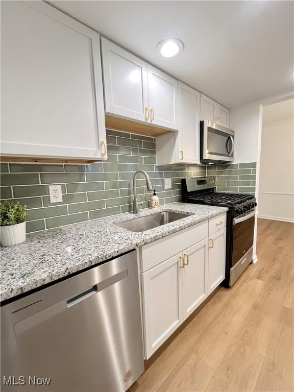 kitchen with light wood-type flooring, stainless steel appliances, light stone counters, white cabinets, and sink