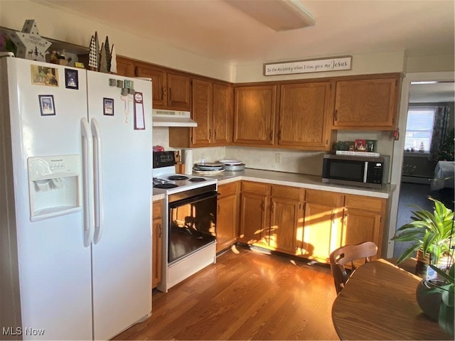 kitchen with stainless steel microwave, under cabinet range hood, light countertops, range with electric stovetop, and white refrigerator with ice dispenser