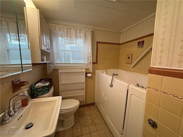 bathroom with a sink, wallpapered walls, tile walls, tile patterned flooring, and a bath