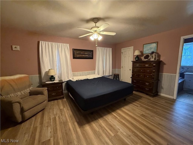 bedroom featuring ceiling fan, wood finished floors, and wainscoting