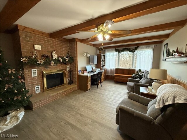 living room featuring ceiling fan, a fireplace, light hardwood / wood-style floors, and beam ceiling