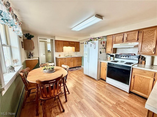 kitchen with light wood finished floors, under cabinet range hood, light countertops, white appliances, and a sink