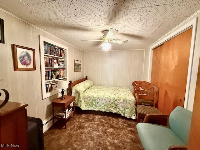 bedroom with a baseboard heating unit, ceiling fan, wood walls, carpet flooring, and a closet