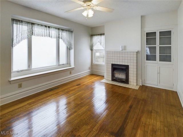 unfurnished living room featuring a tiled fireplace, dark wood-type flooring, and ceiling fan