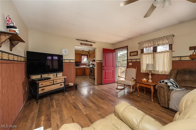 living room with a wainscoted wall, ceiling fan, and dark wood-type flooring