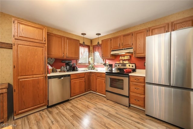 kitchen with light wood-style flooring, appliances with stainless steel finishes, hanging light fixtures, light countertops, and under cabinet range hood