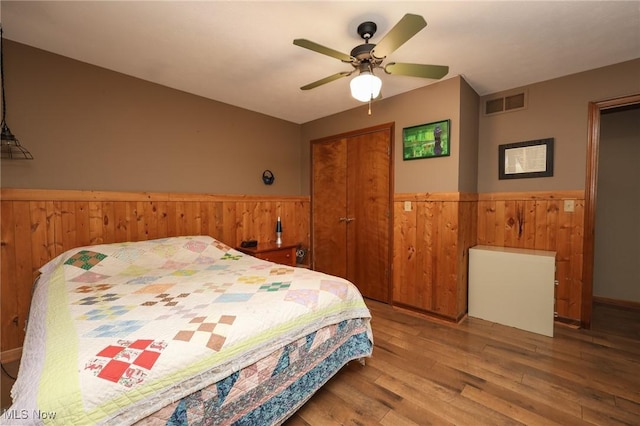 bedroom featuring a wainscoted wall, a closet, visible vents, wooden walls, and wood finished floors