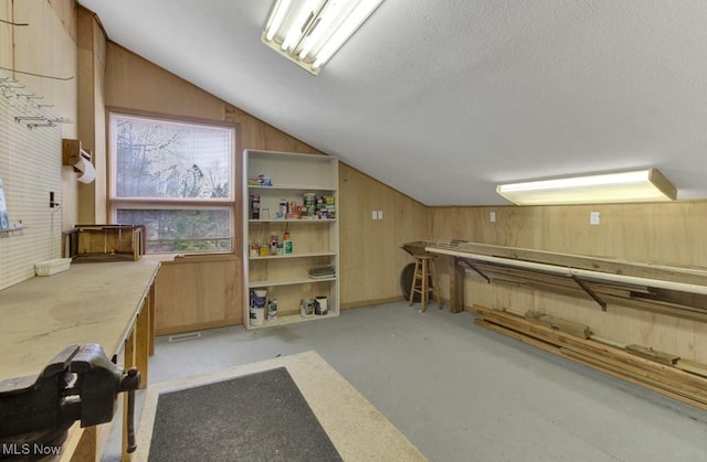 interior space with vaulted ceiling, concrete floors, wood walls, and a textured ceiling