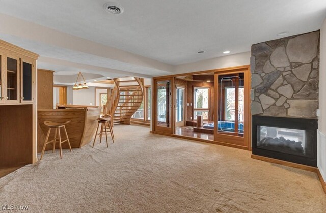 unfurnished living room with bar, a stone fireplace, and carpet floors