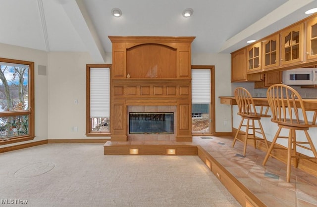 living room featuring a tiled fireplace, light colored carpet, and beamed ceiling