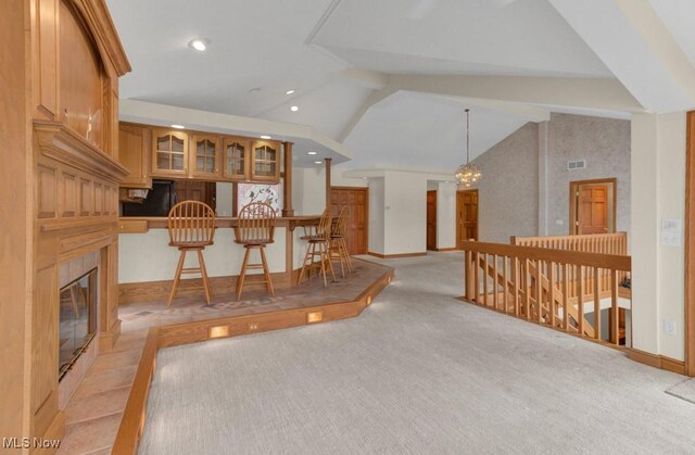 interior space featuring high vaulted ceiling, beamed ceiling, a chandelier, a tiled fireplace, and light colored carpet