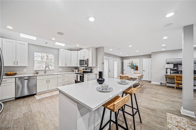 kitchen with stainless steel appliances, white cabinetry, a breakfast bar area, and light hardwood / wood-style flooring