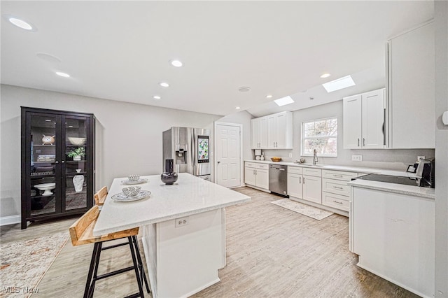 kitchen with a kitchen island, white cabinets, a kitchen bar, stainless steel appliances, and light wood-type flooring