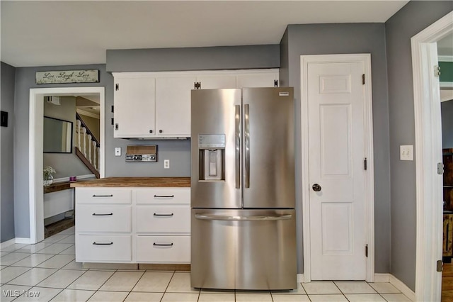 kitchen featuring light tile patterned floors, stainless steel fridge, and white cabinets