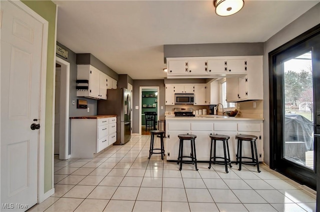 kitchen featuring stainless steel appliances, light tile patterned floors, white cabinets, and a kitchen bar