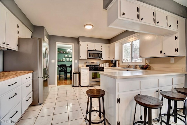 kitchen featuring a breakfast bar area, appliances with stainless steel finishes, white cabinets, light tile patterned flooring, and kitchen peninsula