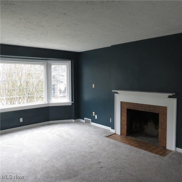 unfurnished living room featuring a tiled fireplace, carpet flooring, and a textured ceiling