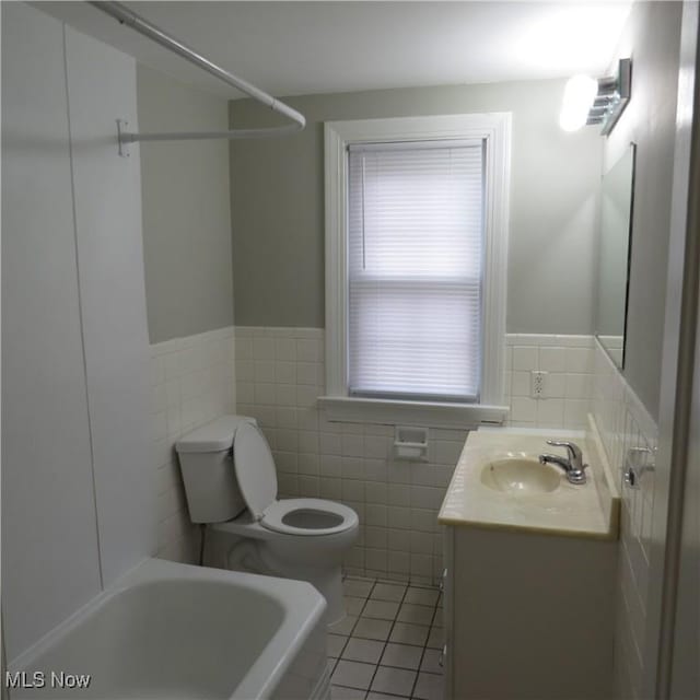 bathroom with toilet, tile walls, vanity, a bathtub, and tile patterned flooring