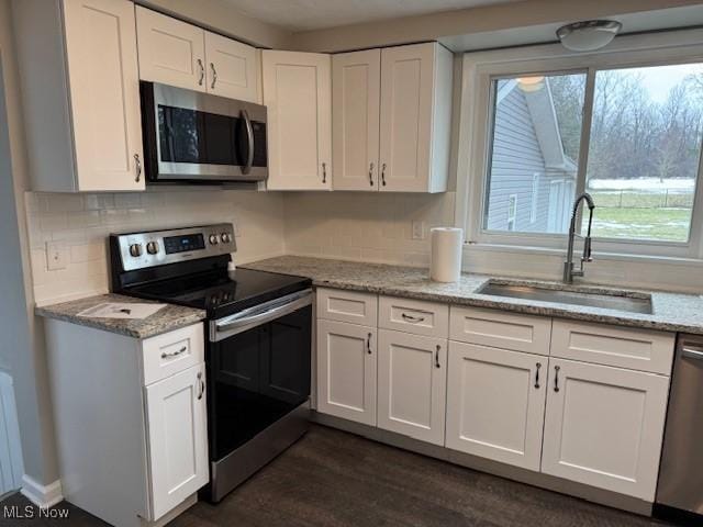 kitchen featuring appliances with stainless steel finishes, white cabinetry, sink, backsplash, and light stone counters