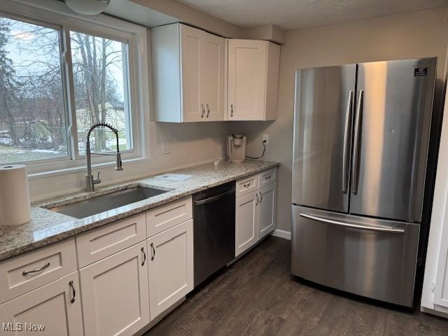 kitchen featuring dishwashing machine, sink, stainless steel fridge, light stone counters, and white cabinets