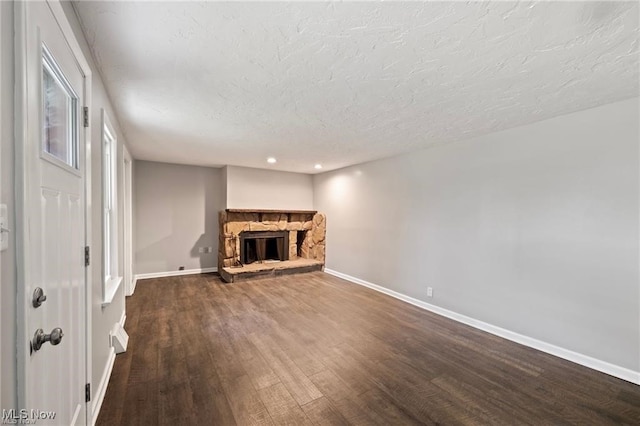 unfurnished living room with a stone fireplace, a textured ceiling, and dark hardwood / wood-style flooring