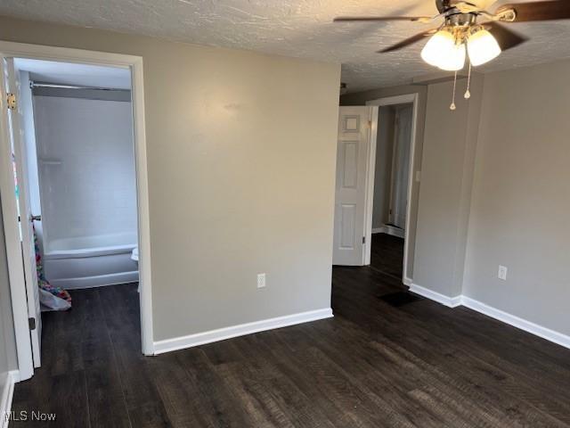 unfurnished bedroom with dark hardwood / wood-style floors, a walk in closet, ceiling fan, a textured ceiling, and a closet