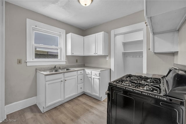 kitchen with black gas range oven, sink, light hardwood / wood-style floors, and white cabinets