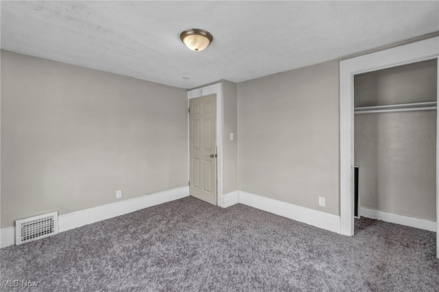 unfurnished bedroom with a textured ceiling, dark carpet, and a closet