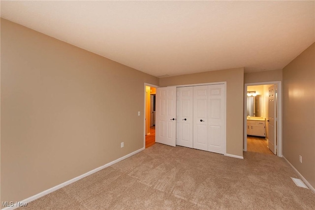 unfurnished bedroom with light carpet, ensuite bath, and a closet