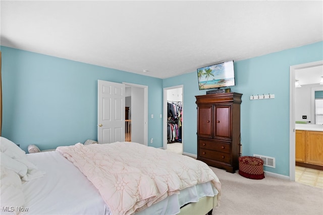 bedroom with a spacious closet, light colored carpet, ensuite bath, and a closet