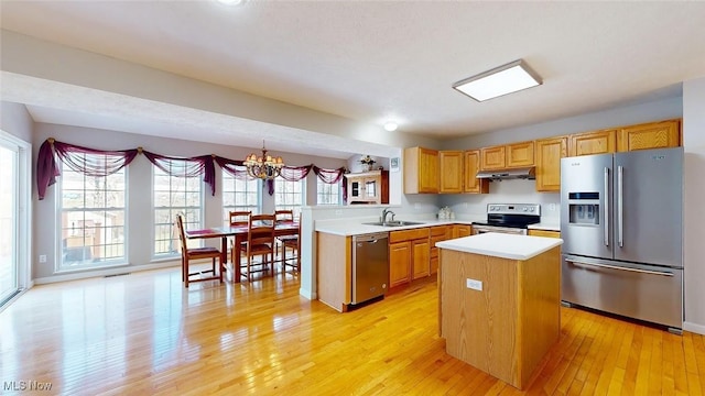 kitchen with appliances with stainless steel finishes, decorative light fixtures, sink, light hardwood / wood-style floors, and kitchen peninsula