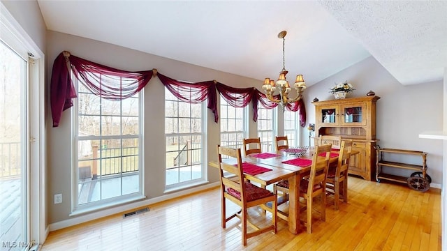 dining space with lofted ceiling, light hardwood / wood-style floors, a textured ceiling, and an inviting chandelier