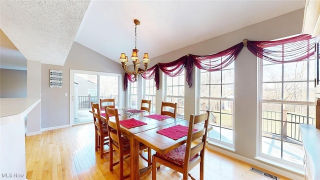 dining room featuring light hardwood / wood-style flooring, a textured ceiling, vaulted ceiling, and a chandelier