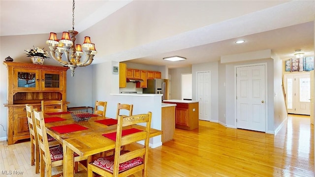 dining area with vaulted ceiling, an inviting chandelier, and light hardwood / wood-style flooring