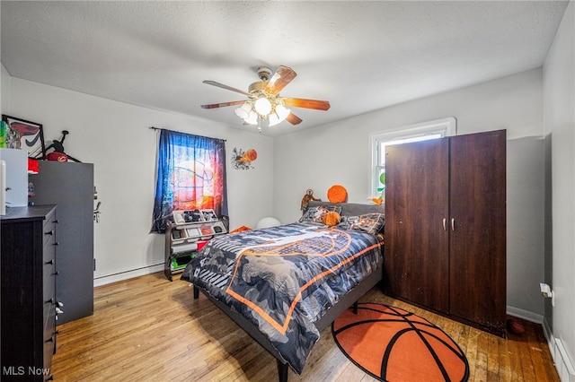 bedroom with ceiling fan, a baseboard radiator, light hardwood / wood-style floors, and a textured ceiling