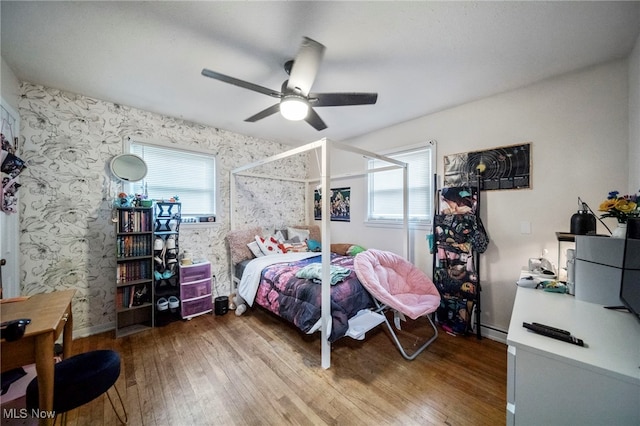 bedroom featuring multiple windows, hardwood / wood-style floors, ceiling fan, and baseboard heating